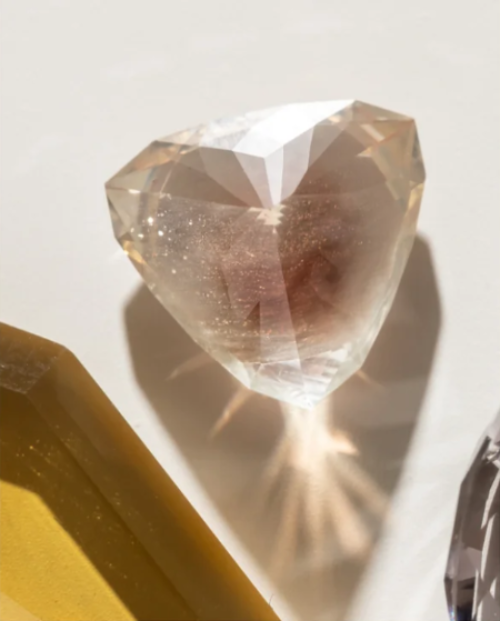 Champagne-colored pear-shaped gemstone catching sunlight, with a gold setting piece beside it