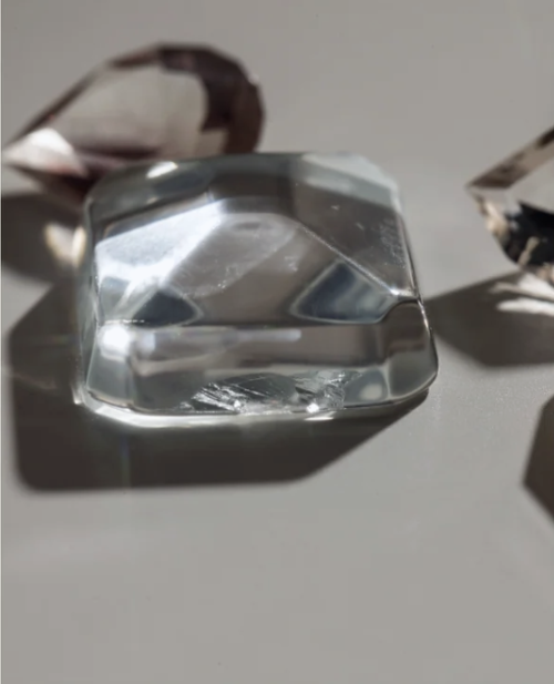 Clear faceted gemstone on a light surface, with additional loose stones blurred in the background